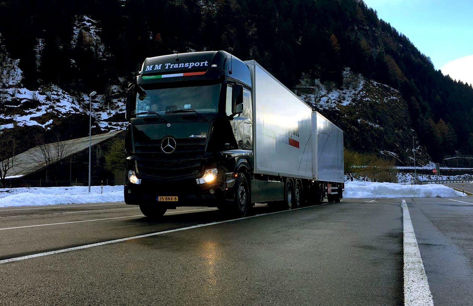 Black M M Transport Mercedes truck with trailer on a snowy mountain road
