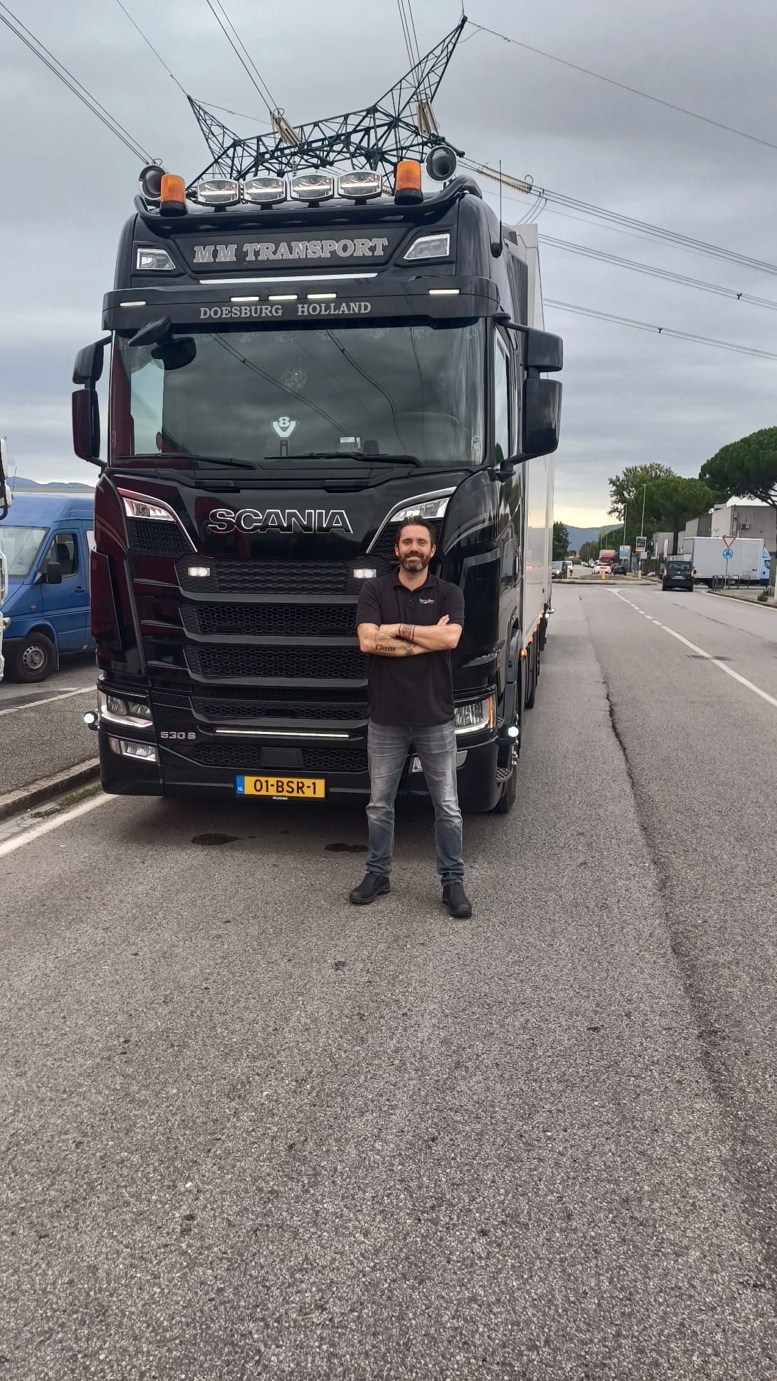 M M Transport driver in front of a black Scania reading ‘M M Transport · Doesburg Holland’ in Italy